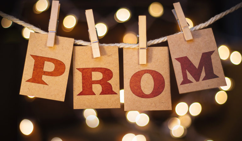 The word PROM printed on clothespin clipped cards in front of defocused glowing lights.